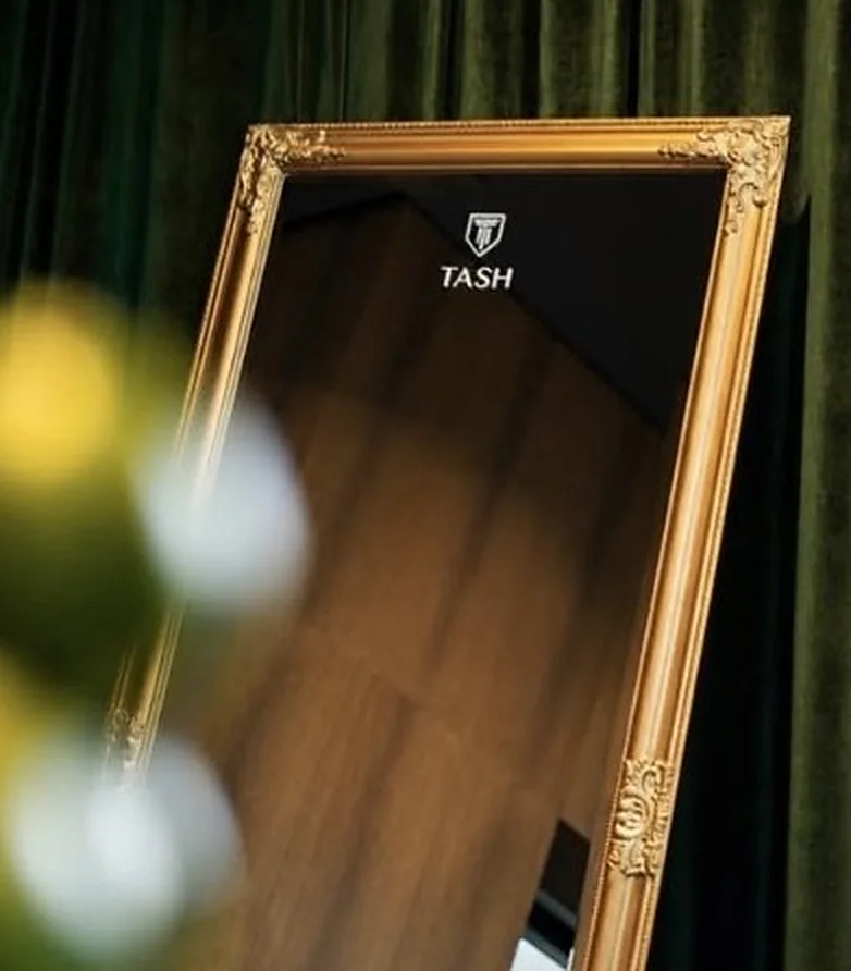 Goldgerahmter Spiegel mit TASH-Branding vor grünem Samtvorhang